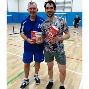 Two men holding awards in a gymnasium.