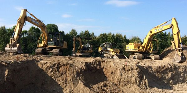 SJS excavators, mini excavator and skid steer lined up in front of large hole