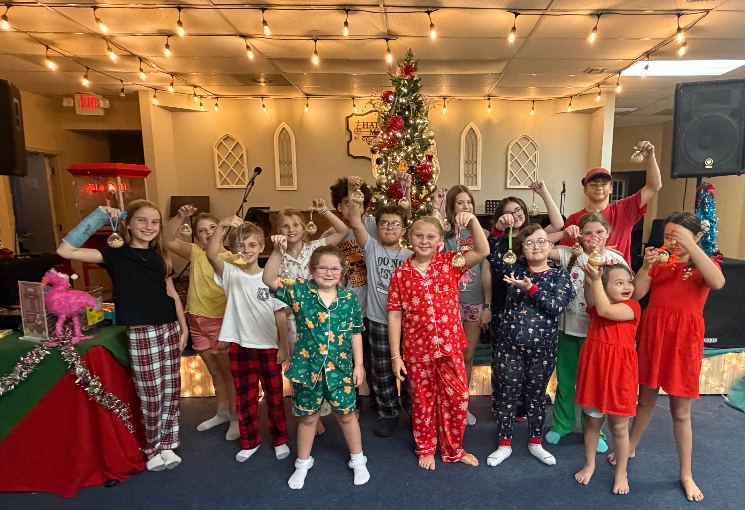 Group of kids holding Christmas ornaments in a festive room.