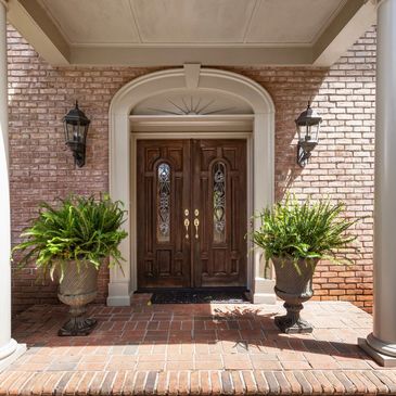 Elegant wooden front door with potted plants on brick porch.