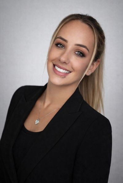 Smiling woman in black blazer with a lip piercing and heart necklace.