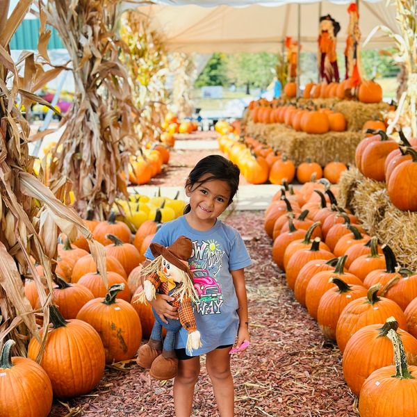 Smiling child holding a scarecrow doll at a pumpkin patch.