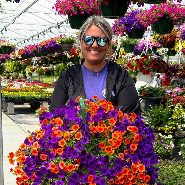 Woman holding vibrant purple and orange flowers in a greenhouse.