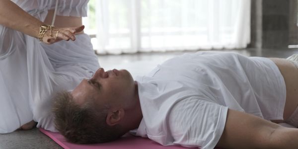 A woman in white performs a healing ritual over a man lying on a yoga mat.