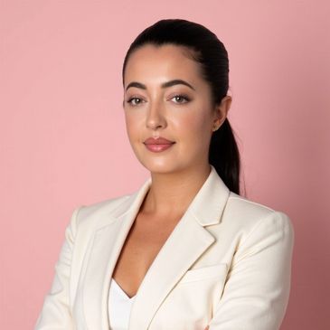 Confident woman in white blazer poses against a pink background.