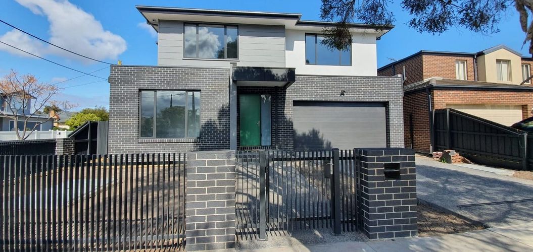 Modern two-story house with black brick facade and metal fence.