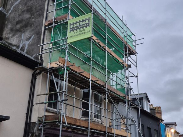 large scaffolding to the front of a shop fully boarded and fitted with green safety netting.