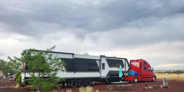 Large white trailer attached to a red truck under cloudy skies.