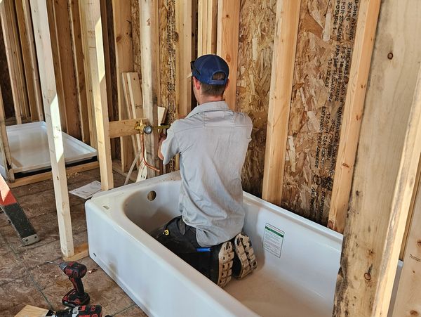 Worker installing plumbing in a bathtub.