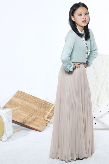 Woman in pastel green blouse and beige pleated skirt posing indoors.