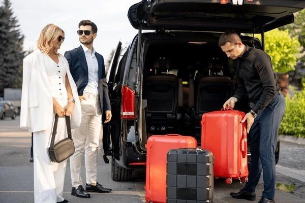 Stylish people with luggage next to a black van, preparing for a trip.