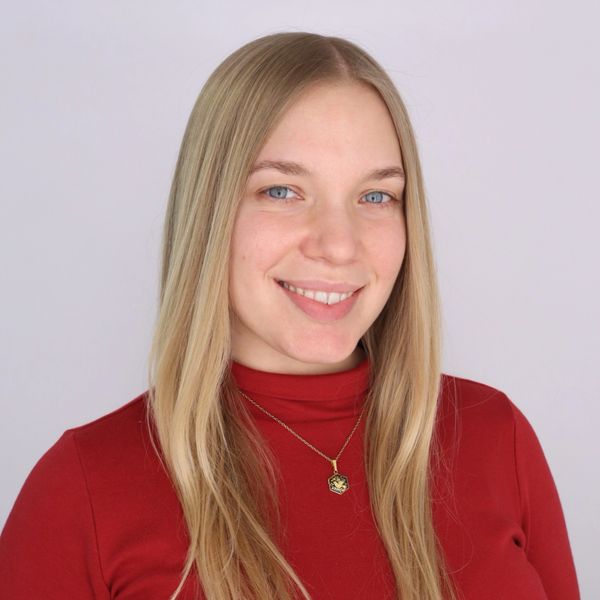 Smiling young woman with long blonde hair wearing a red top and pendant necklace.