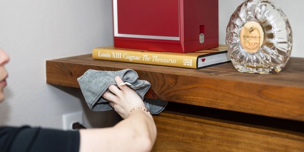 Person cleaning a wooden shelf with a cloth.