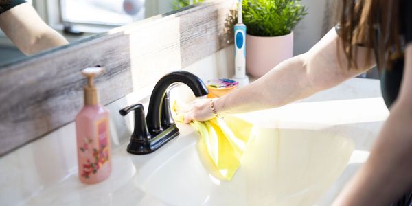 Person cleaning bathroom sink with a yellow cloth.