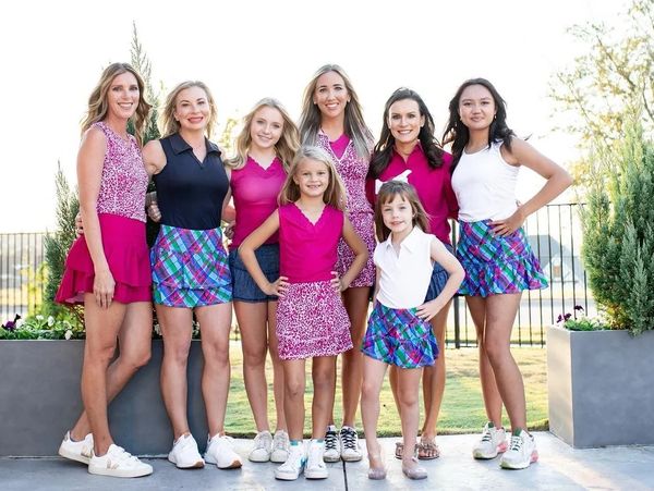 Group of women and girls in colorful tennis skirts posing outdoors.
