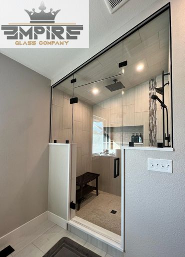 Modern glass shower enclosure with black hardware and wooden bench inside.