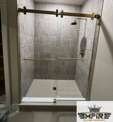 Modern glass shower enclosure with gold fixtures and tiled walls.
