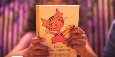 Enfant qui lit le dos du livre “Elena et les mitaines magiques”.