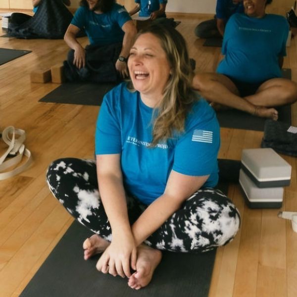 Woman in blue shirt laughing during a yoga session on a mat.