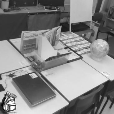 Desks arranged to make a large rectangle with books, a computer and a globe displayed on top. 