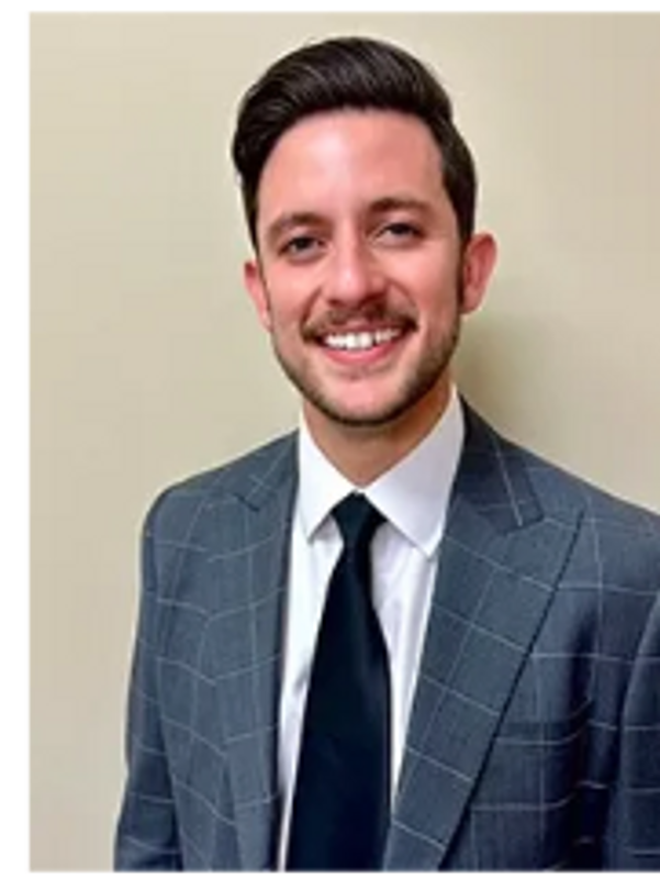 A young man in a checkered suit and black tie smiling.