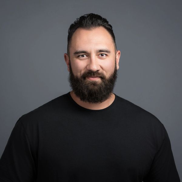 Smiling man with beard and black shirt against gray background.