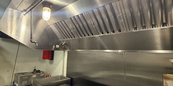 Clean commercial kitchen grill with stainless steel hood and lights.