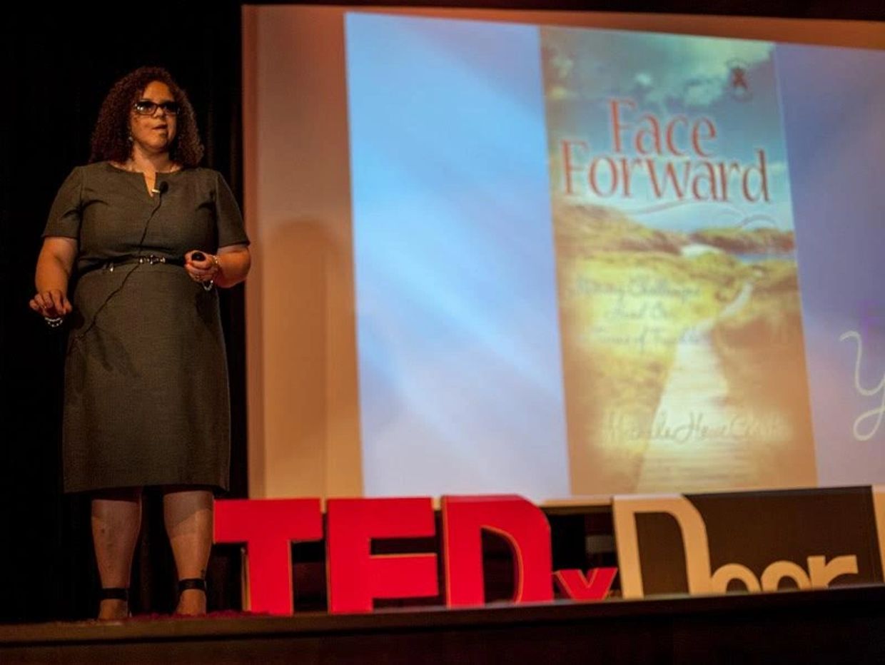 Goddess Alchemy and Meditation Magic Teacher stands on TEDx stage with her book Face Forward