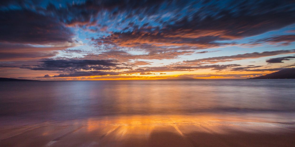 Sunset over a calm beach with colorful clouds.