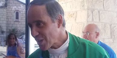Man wearing a green clergy robe speaking outdoors.