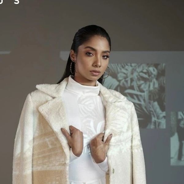 Woman in a white coat posing confidently.