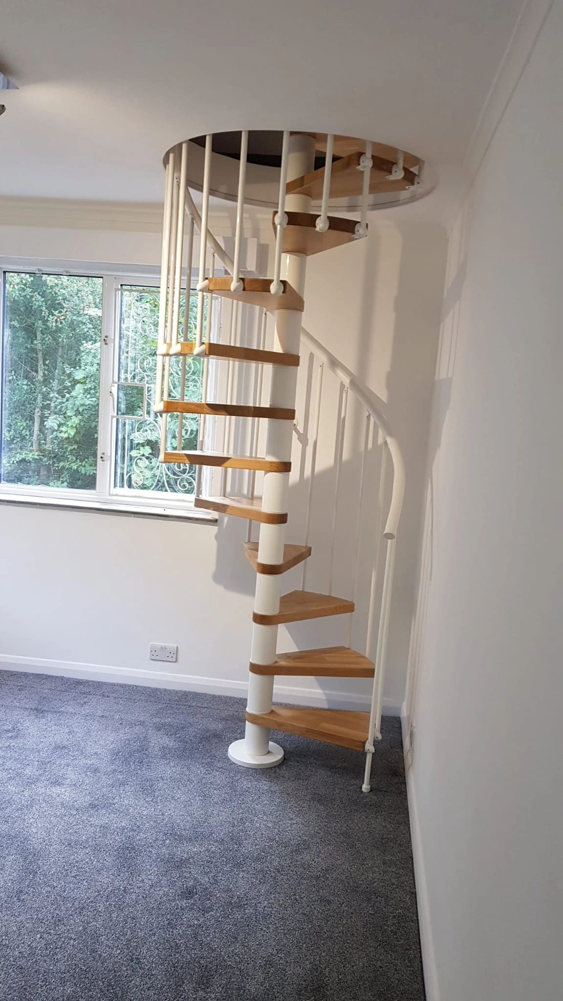 Modern spiral staircase with wooden steps and white railings in a bright room.
