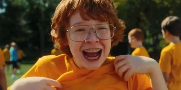 A cheerful boy with glasses wearing an orange shirt outdoors.