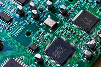 Close-up of a green printed circuit board with multiple integrated circuits and capacitors.