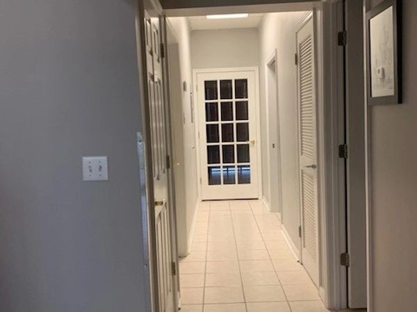 A clean, well-lit hallway with white walls and tiled floor leading to a glass-paneled door.