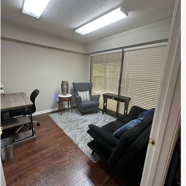 Cozy, minimalist office with a desk, armchair, couch, and window blinds.
