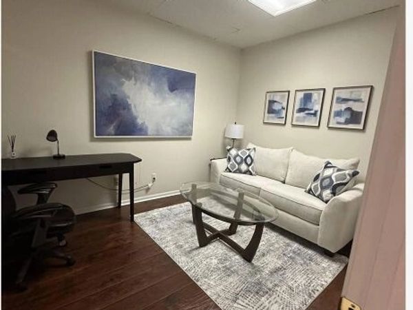 Modern office with a white couch, glass coffee table, and abstract wall art.