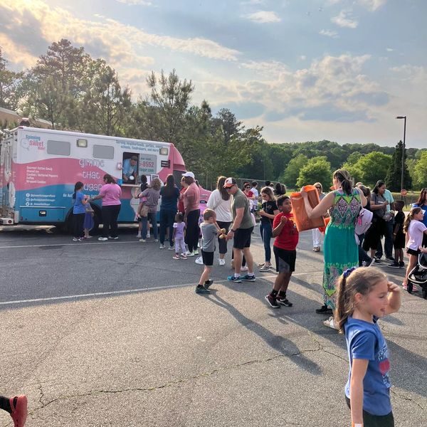 Families and children gather around a colorful cotton candy truck on a sunny day.