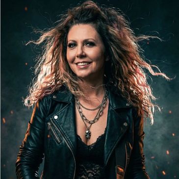 Confident woman with curly hair in a black leather jacket and layered necklaces.