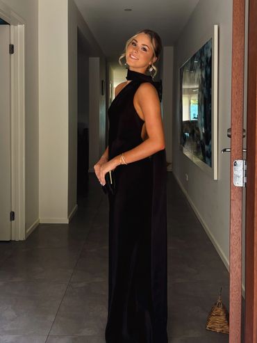 Woman in elegant black evening gown posing indoors with a smile.