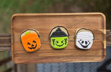 Three Halloween-themed decorated cookies on a wooden tray.