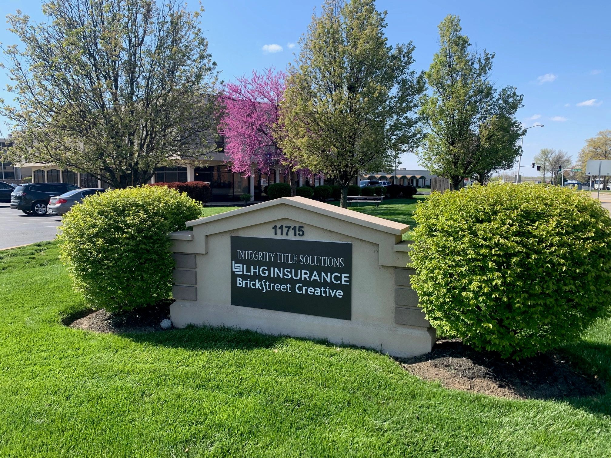 Office sign surrounded by green and blossoming trees.