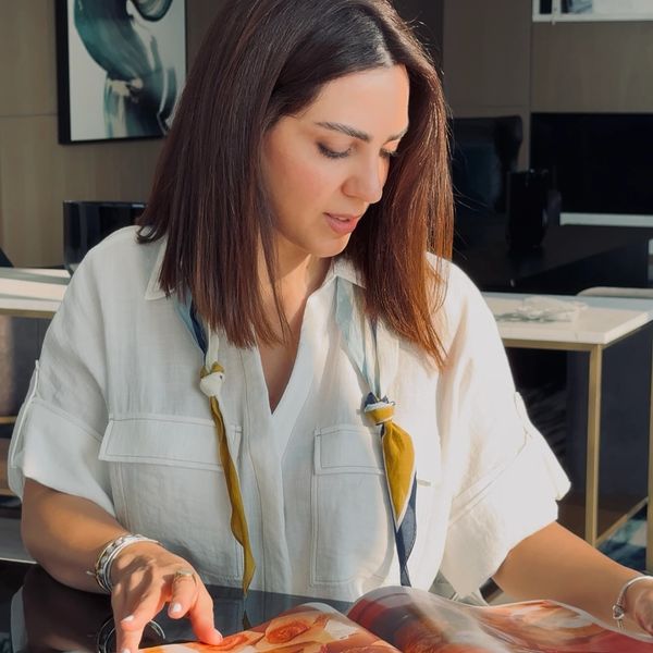 A woman in a white shirt reading a magazine at a reflective black table.