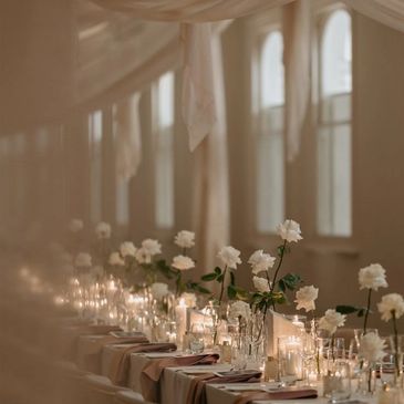 Elegant table setting with white roses and candles under soft drapes.