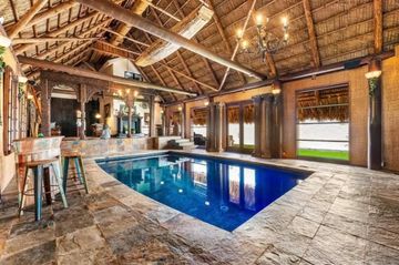 Luxurious indoor pool with rustic thatched roof and stone flooring.