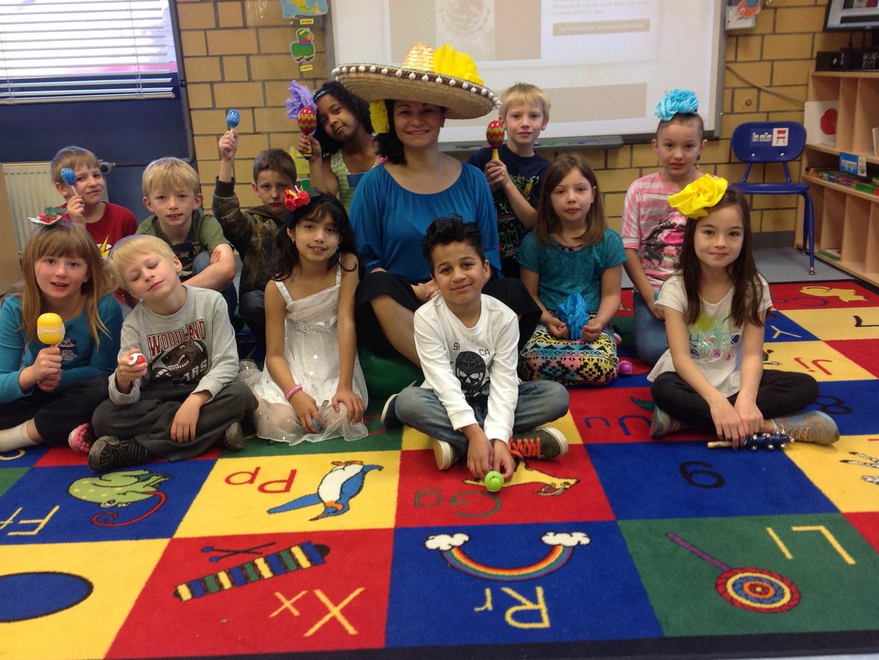 Group of children and teacher in classroom with colorful carpet.
