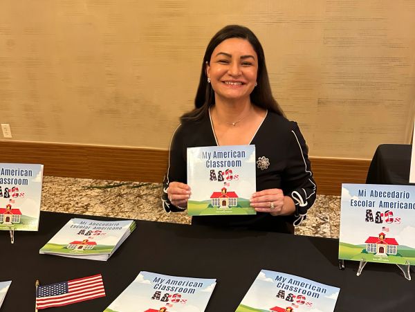 Woman smiling, holding a book titled 'My American Classroom ABCs'.