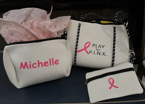 Three white bags with pink breast cancer awareness ribbons and text.