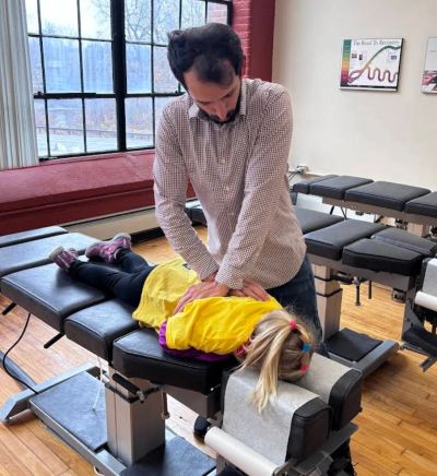 A man performs chiropractic adjustment on a young girl lying on a treatment table.