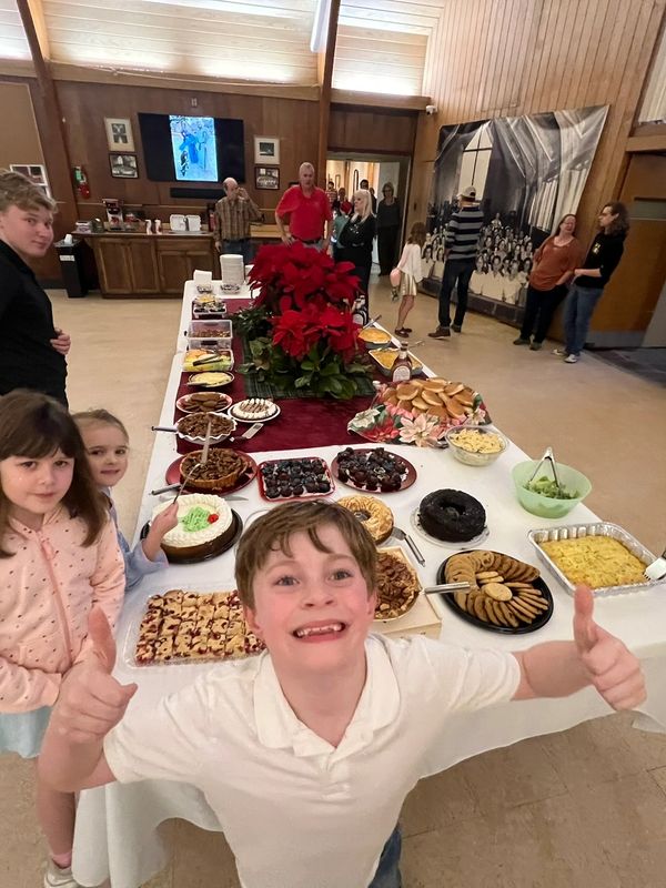 Happy kids and adults gathered around a festive buffet table filled with desserts and snacks.